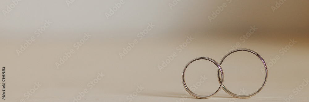 Two gold wedding rings intertwined on a neutral beige surface, symbolizing unity and eternal love. Ideal for wedding or anniversary concepts. Banner with copy space. Two gold wedding rings intertwined on a neutral beige surface, symbolizing unity and eternal love. Ideal for wedding or anniversary concepts. Banner with copy space.
