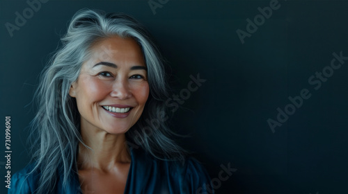 Happy smiling stylish confident 50 years old Asian female professional standing looking at camera at gray background. Portrait of sophisticated grey hair woman advertising products.