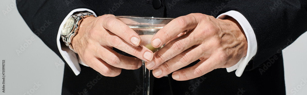 cropped view of glass of delicious martini with green olives in it in hands of mature man, banner