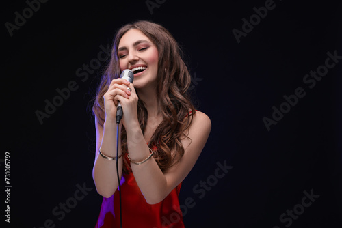 Emotional woman with microphone singing in color light on black background. Space for text
