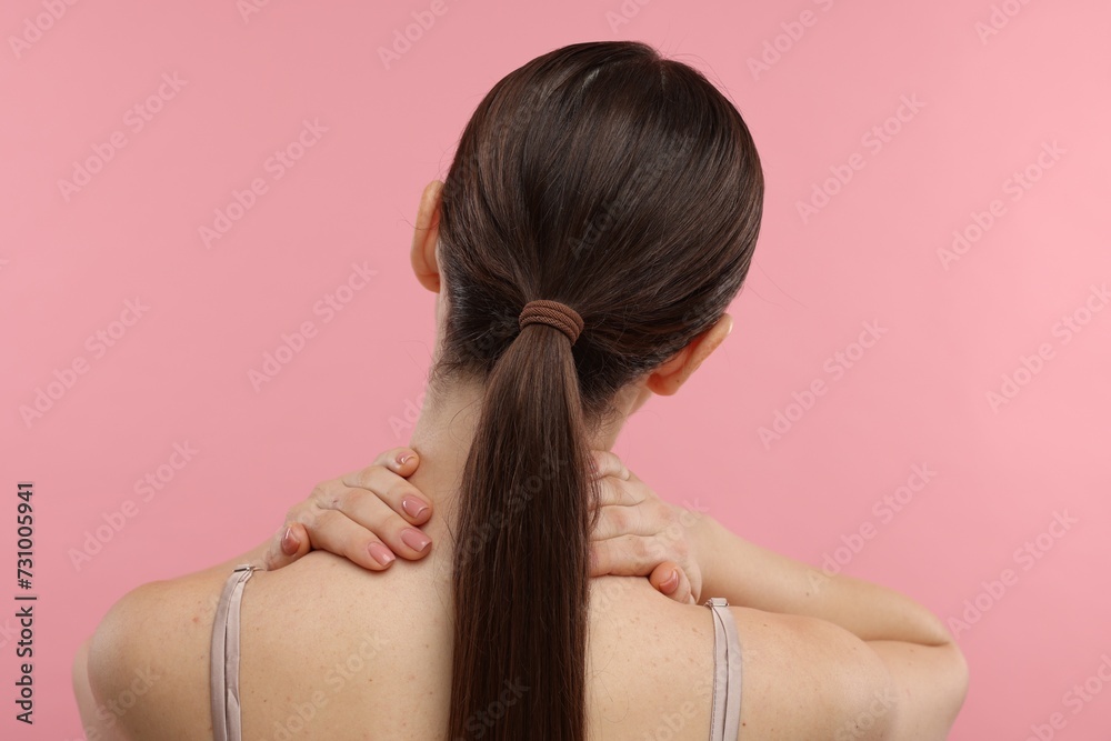 Fototapeta premium Woman touching her neck on pink background, back view