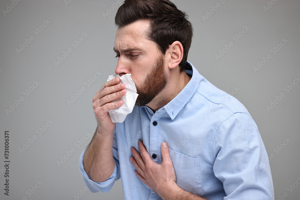 Sick man with tissue coughing on light grey background Sick man with tissue coughing on light grey background