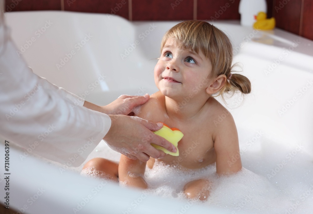 Mother washing her little daughter with sponge in bathtub, closeup Mother washing her little daughter with sponge in bathtub, closeup