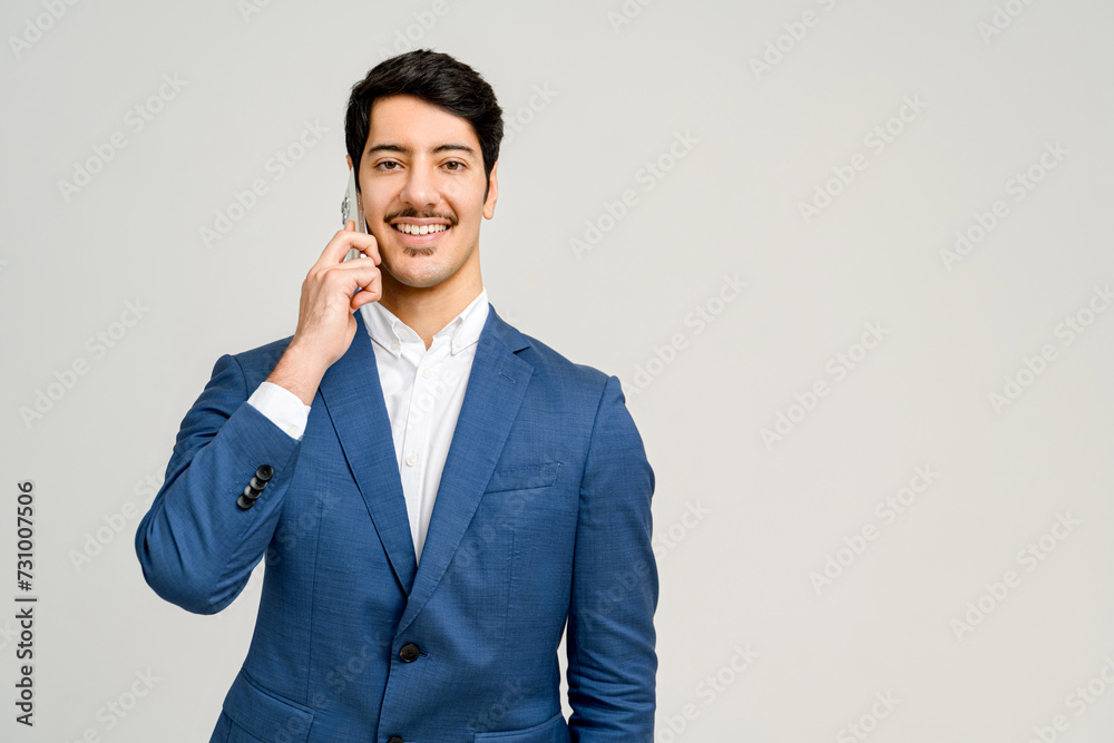 Professional portrait of a man in a blue business suit is engaged in a phone conversation, smiling and looking at camera, suggesting a successful business dialogue or client interaction Professional portrait of a man in a blue business suit is engaged in a phone conversation, smiling and looking at camera, suggesting a successful business dialogue or client interaction