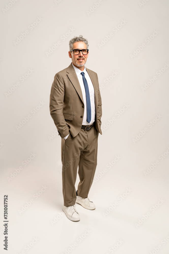 Full body portrait of a senior businessman in a beige suit and casual white sneakers, standing confidently with hands in pockets, blending traditional business attire with a modern twist. Full body portrait of a senior businessman in a beige suit and casual white sneakers, standing confidently with hands in pockets, blending traditional business attire with a modern twist.