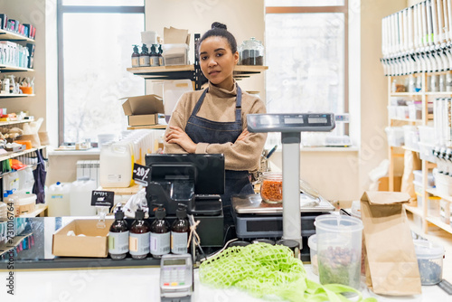Portrait of confident African American woman owner of local zero waste grocery store wearing apron at cash desk