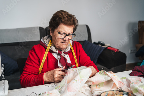 older woman in her living room cutting a piece of fabric with sewing scissors to create a dress