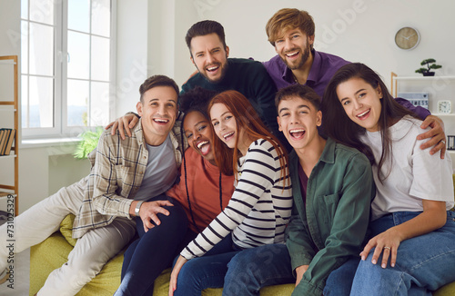 Group of young people sits on a sofa at home together, sharing moments of laughter and happiness. Portrait of a diverse camaraderie of friends, smiling and looking into the camera.