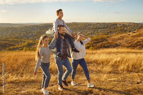 Happy smiling young family with son and daughter walking outdoors enjoying beautiful nature in the field. Mother, father with two kids hiking at sunny day together. Family leisure concept.