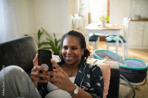 Smiling young woman using smartphone on home sofa photo