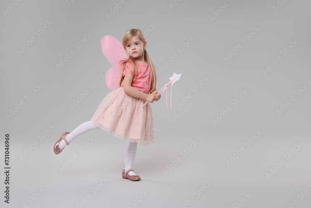 Cute little girl in fairy costume with pink wings and magic wand on light grey background, space for text Cute little girl in fairy costume with pink wings and magic wand on light grey background, space for text