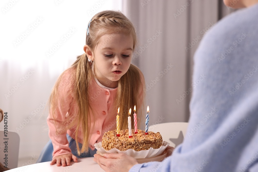 Birthday celebration. Mother holding tasty cake with burning candles near her daughter indoors Birthday celebration. Mother holding tasty cake with burning candles near her daughter indoors