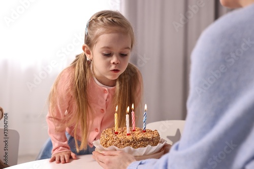 Birthday celebration. Mother holding tasty cake with burning candles near her daughter indoors