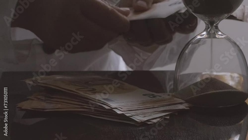 closeup female hands count 50 euro banknotes of european union against background of scattered paper banknotes on table, hourglass, concept Time is money, money laundering, financial scam photo