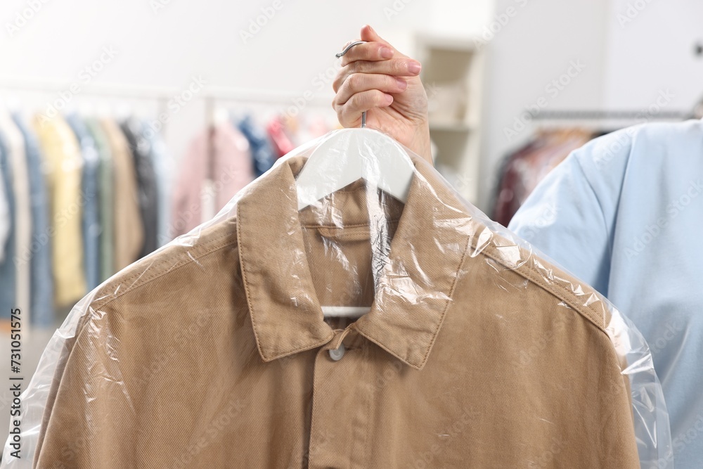 Dry-cleaning service. Woman holding shirt in plastic bag indoors, closeup Dry-cleaning service. Woman holding shirt in plastic bag indoors, closeup