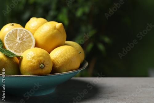 Fresh lemons and green leaves on grey table outdoors  closeup. Space for text