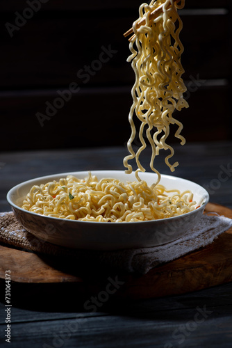 man takes a portion of hot noodles with chopsticks, dark background, closeup