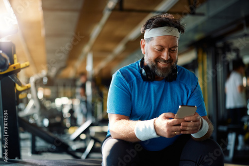 Happy mature man using smart phone on break during gym workout.