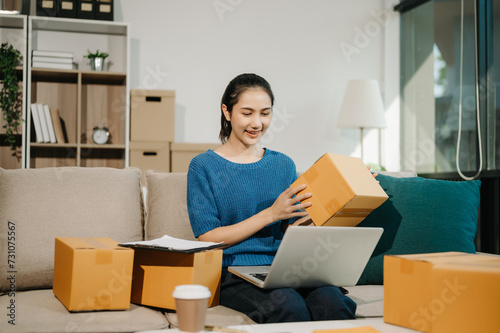 Young business owner woman prepare parcel box and standing check online orders for deliver to customer on sofa Shopping Online concept.