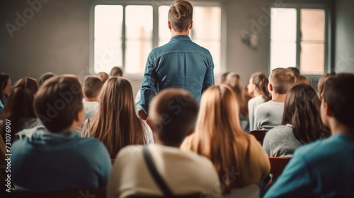 In the classroom  a large group of students listens attentively to their high school teacher  with focus on a boy in the middle.