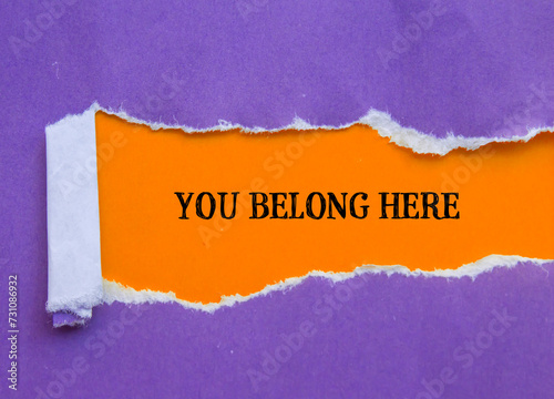 You belong here lettering on purple torn paper with orange background. Conceptual business symbol. Copy space. photo