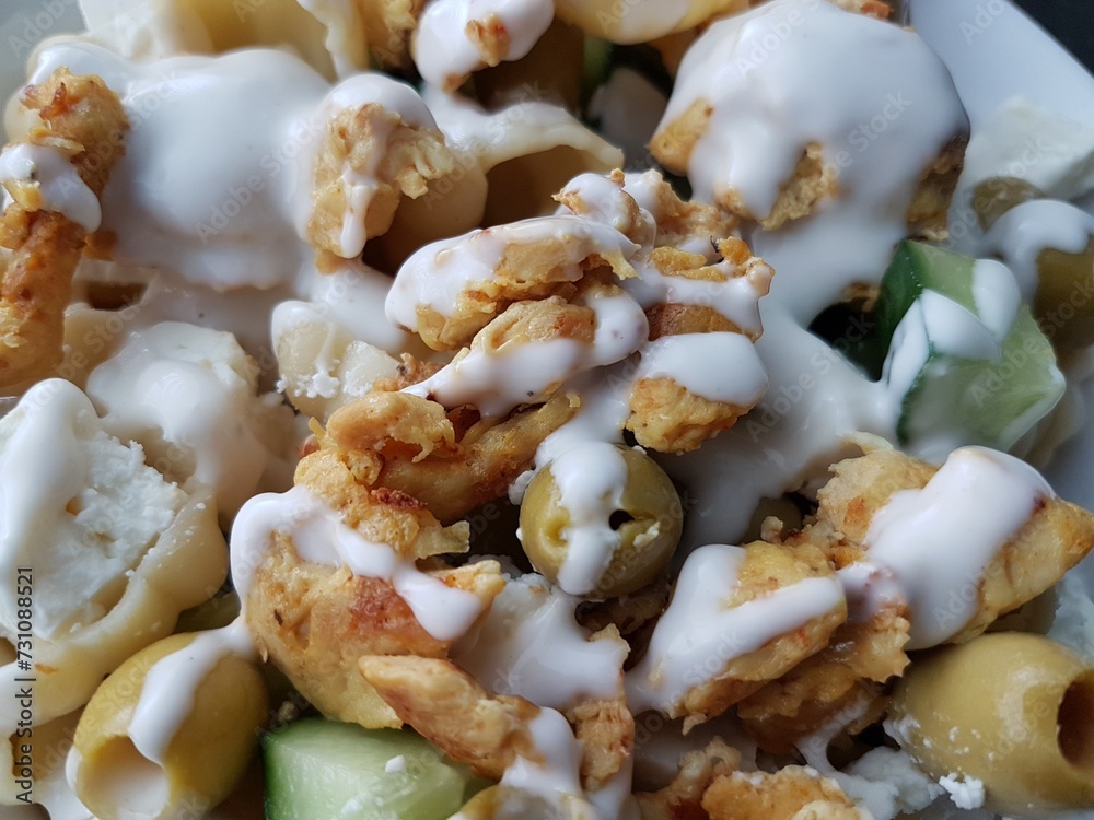 Close-up of a salad with chicken, cucumber, pasta, green olives and dressing on a white plate Close-up of a salad with chicken, cucumber, pasta, green olives and dressing on a white plate