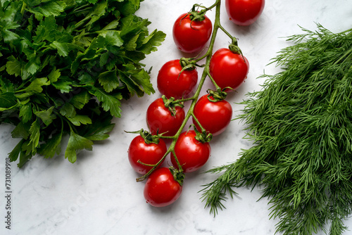 Close up of cherry tomatoes with bunch of parsley and dill on marble tabletop...