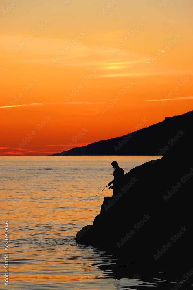 Unrecognizable person fishing on the beach at sunset. Beautiful landscape in Brela, Croatia.