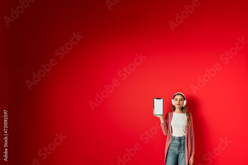 jeune adulte ou adolescente femme avec des écouteurs sur les oreilles et une tablette à la main. Concept de sites numériques de musique. Fond rouge avec espace négatif pour texte copyspace photo