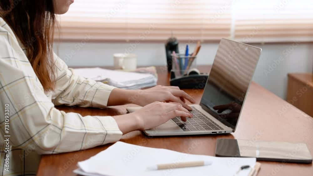 Asian women's hands resting on laptop computers, hand touching computer slowly, typing in various work information slowly carefully, there is work equipment, many documents are on desks in office. Asian women's hands resting on laptop computers, hand touching computer slowly, typing in various work information slowly carefully, there is work equipment, many documents are on desks in office.