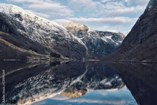 Bergen Fjord, Norway. The clear lake water reflects the sunset and snow-capped mountains like a mirror.
