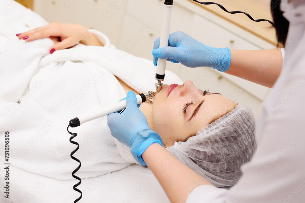 Obraz premium cosmetologist conducts microcurrent facial therapy for a young woman using a device in a beauty salon. Hardware cosmetology, skin care, rejuvenation, regeneration.