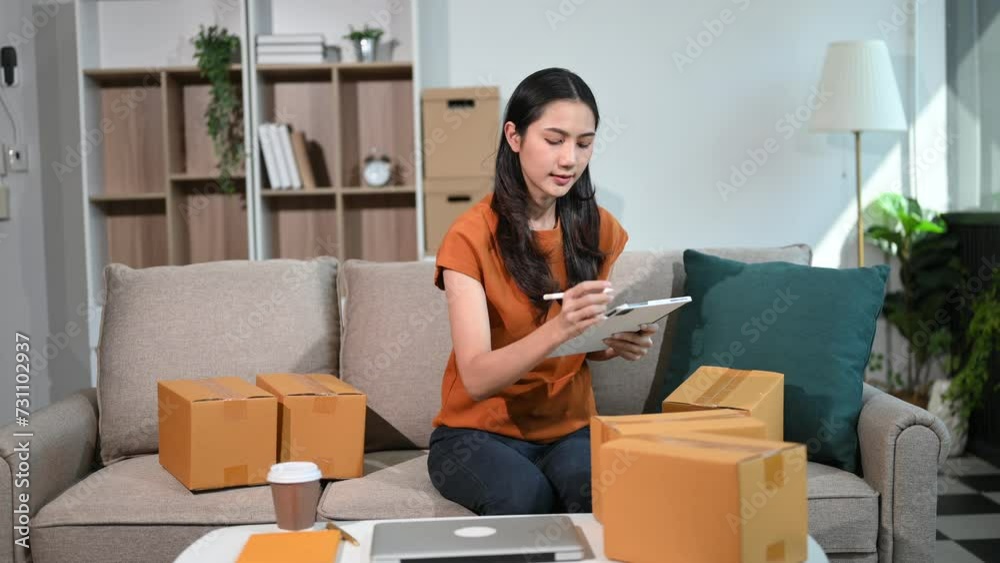 Startup small business SME woman using smartphone or tablet taking receive and checking online purchase shopping order to preparing pack product box. on sofa at home office Startup small business SME woman using smartphone or tablet taking receive and checking online purchase shopping order to preparing pack product box. on sofa at home office