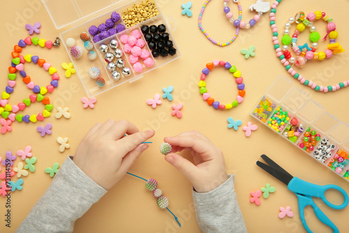Little girl made bracelets on beige background. Kids handmade beaded jewelry. DIY bracelet beads.