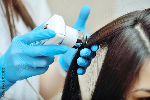 doctor cosmetologist dermatologist diagnoses the condition of the patient's hair using a special device - a trichoscope. photo