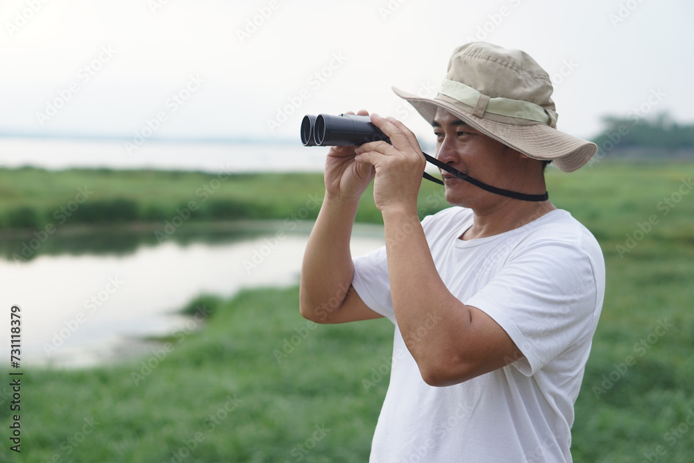Handsome Asian man ecologist is surveying nature at the lake, hold binoculars. Concept, nature exploration. Ecology study. Pastime activity, lifestyle. Explore environment      