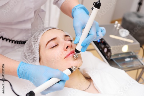 Fototapeta Naklejka Na Ścianę i Meble -  cosmetologist conducts microcurrent facial therapy for a young woman using a device in a beauty salon. Hardware cosmetology, skin care, rejuvenation, regeneration.