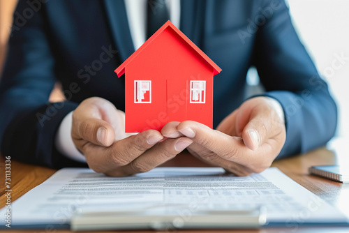 Hands of real estate agent or bank manager holding red house in office. Home Insurance, banking, property investment and mortgage loan concept