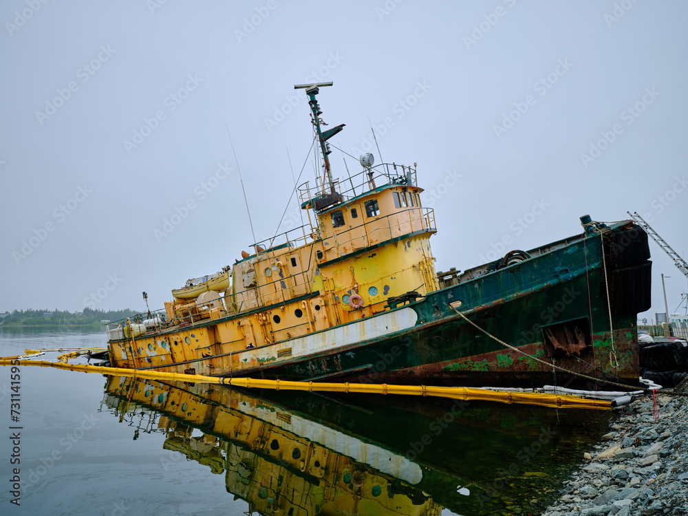 Large rusting tugboat listing and sinking on its starboard side in Hawbolt Cove in Halifax Nova Scotia Large rusting tugboat listing and sinking on its starboard side in Hawbolt Cove in Halifax Nova Scotia