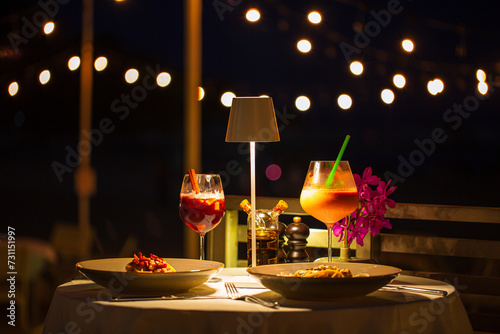beachside dinner table,Beachside dinner table with one large challah, two bottles of red wine, two wine glasses, two tea lights in jars, one small vase with flowers, at night, with hanging light nearb photo