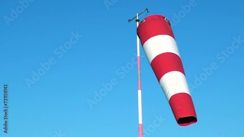 video of a wind sleeve to signal wind direction and intensity positioned at a small parachute airfield, isolated against a blue sky