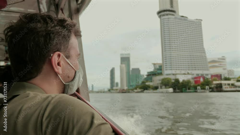Man wearing face mask looks out at city skyline from boat. Urban travel and health safety. Man wearing face mask looks out at city skyline from boat. Urban travel and health safety.
