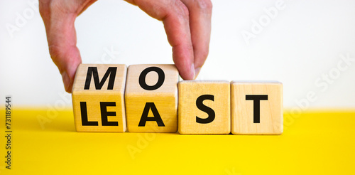 Most or least symbol. Businessman turns beautiful wooden cubes and changes the word Least to Most. Beautiful yellow table white background. Copy space. Business and most or least concept.