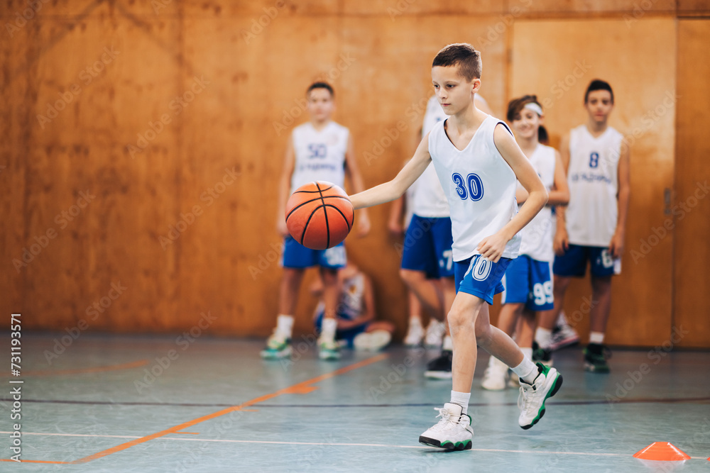 A junior basketball player is practicing ball dribbling on court.