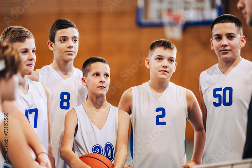 A junior basketball players standing on court and listening coach. photo