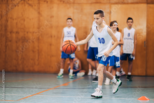 A junior basketball player is practicing ball dribbling on court.
