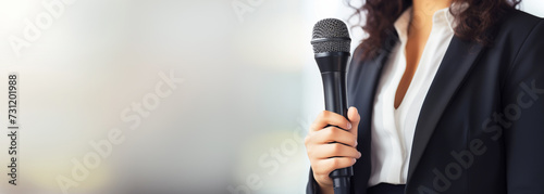 Motivational female speaker with microphone speaking on stage, banner format