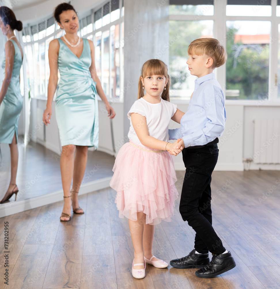 Obraz premium Passionate tween dancers, girl and boy practicing ballroom dancing in dance studio, gracefully performing waltz while female trainer monitoring technique and progress..