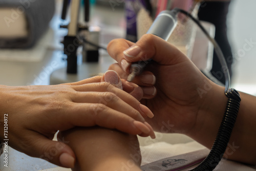 Fotografie Beautician filing nails with an electric filer to a woman in a beauty center