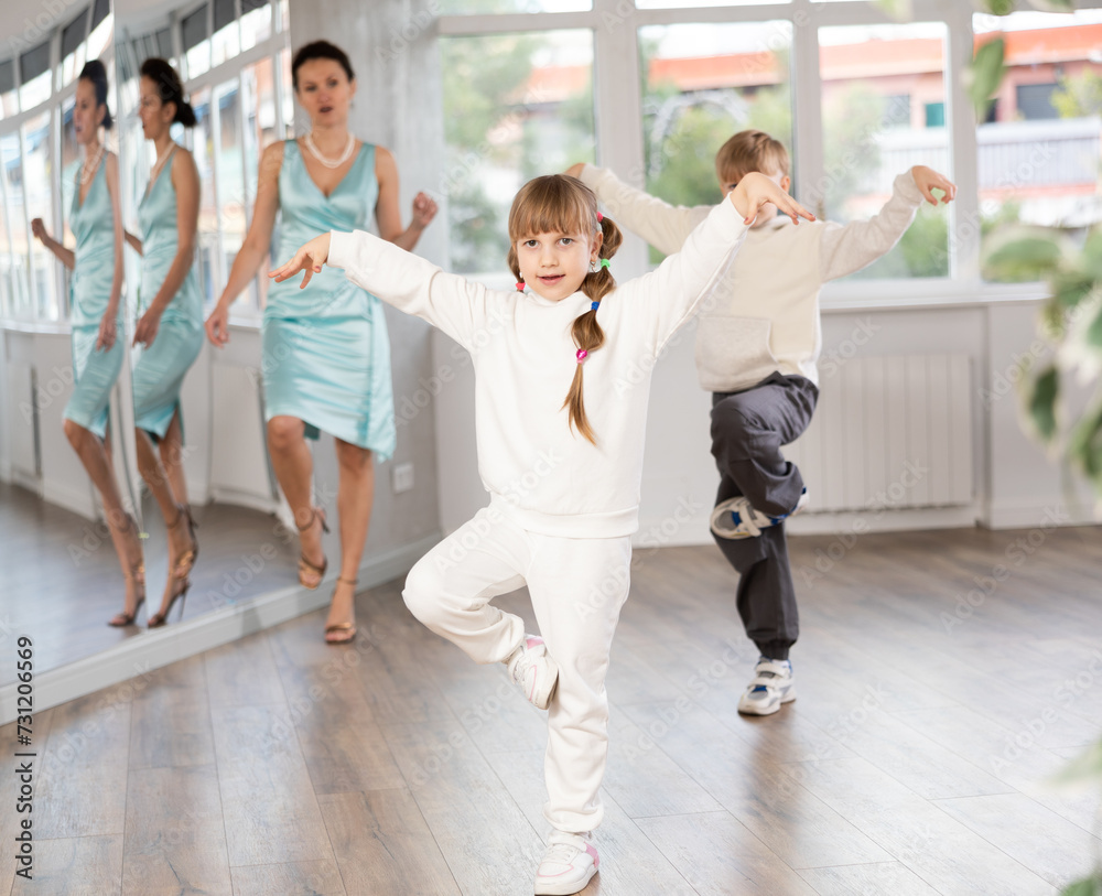 Fototapeta premium Cheerful preteen girl and boy enjoying modern dancing during lesson in dance studio, practicing hip-hop movements under guidance of female teacher..